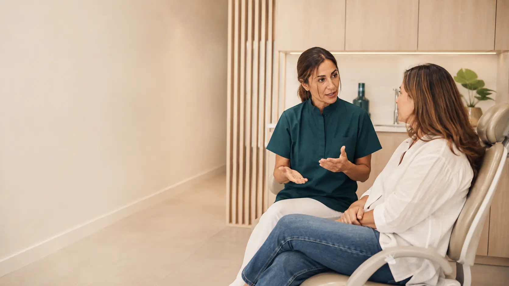 Profesional conversando con una paciente en una cl&iacute;nica dental luminosa